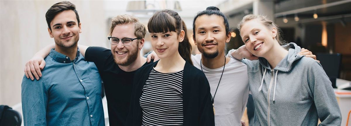 Five developers in their twenties are standing in a row with their arms around each other's shoulders. They are smiling at the camera.