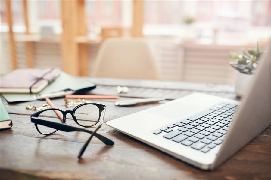 An open laptop on a desk. A pair of glasses are lying next to the laptop.