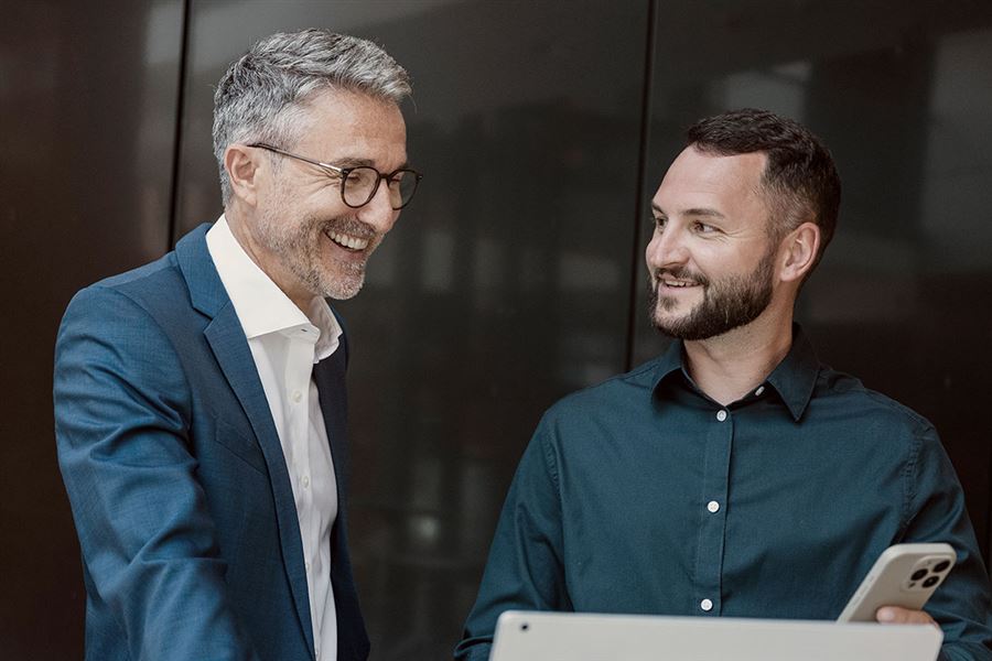 Two colleagues have a stand-up meeting while looking at a computer.