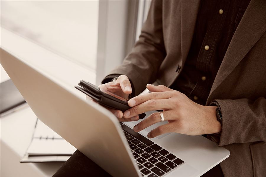Hands of a man who's using a mobile while having a laptop in front of him. 