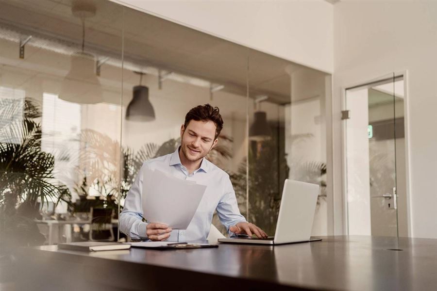A man is working in an office. He is sitting in a conference room with a laptop in front of him.