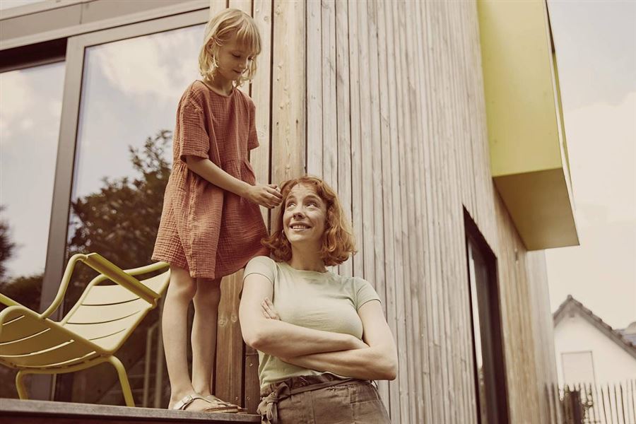 En kvinna står utanför ett hus. Hennes dotter står på en altan bredvid. 